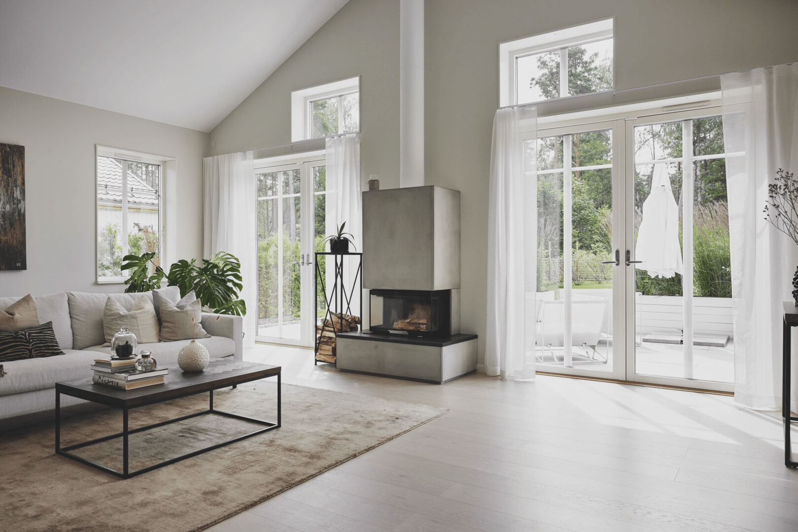 Ljust skandinaviskt vardagsrum med stora vitmålade fönster och altandörrar mot trädgården.