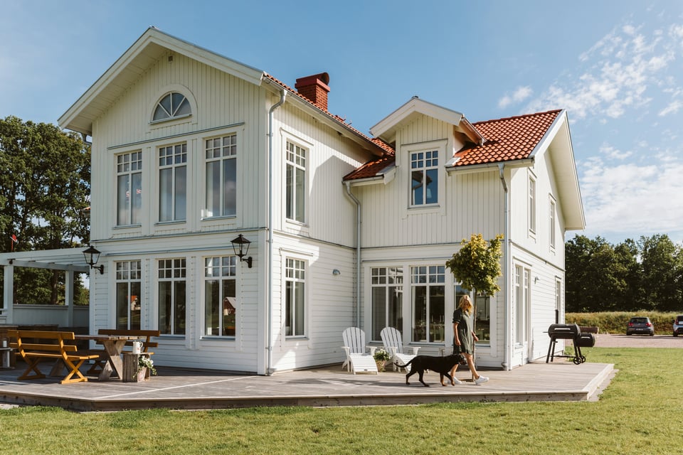 Vit hus med stora fönster, gräsmatta och blå himmel mitt i sommaren