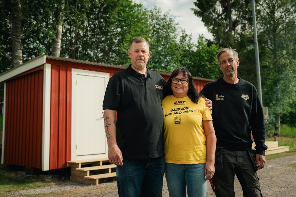 Bild på 3 personer framför ett rött hus